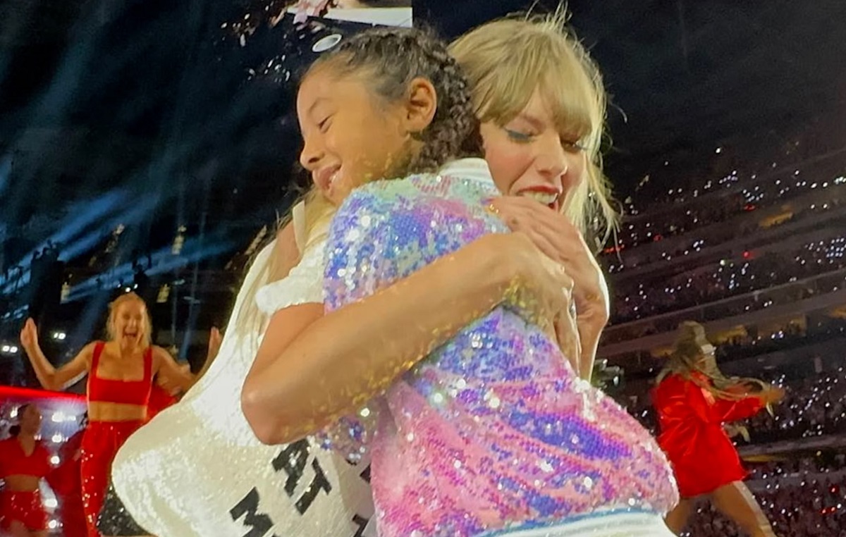 Exclusive: Taylor Swift trots up to a young fan belting out her song lyrics. After giving the girl a sweet hug, Swift hands her the coveted 22 trilby, causing the young fan to burst into happy tears...